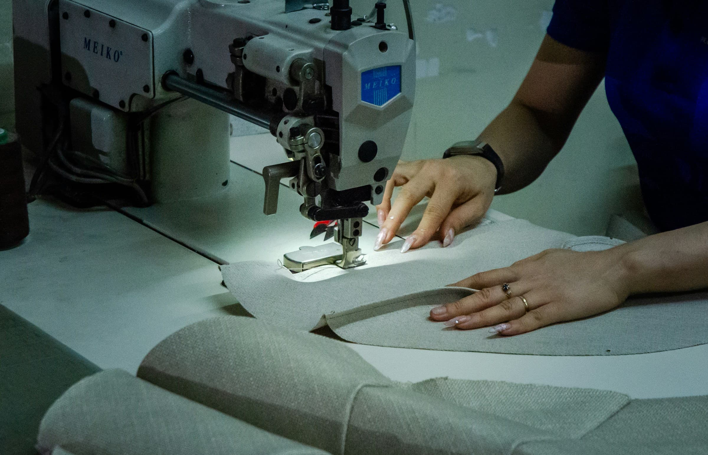 Hands guiding fabric under the needle of an industrial sewing machine.