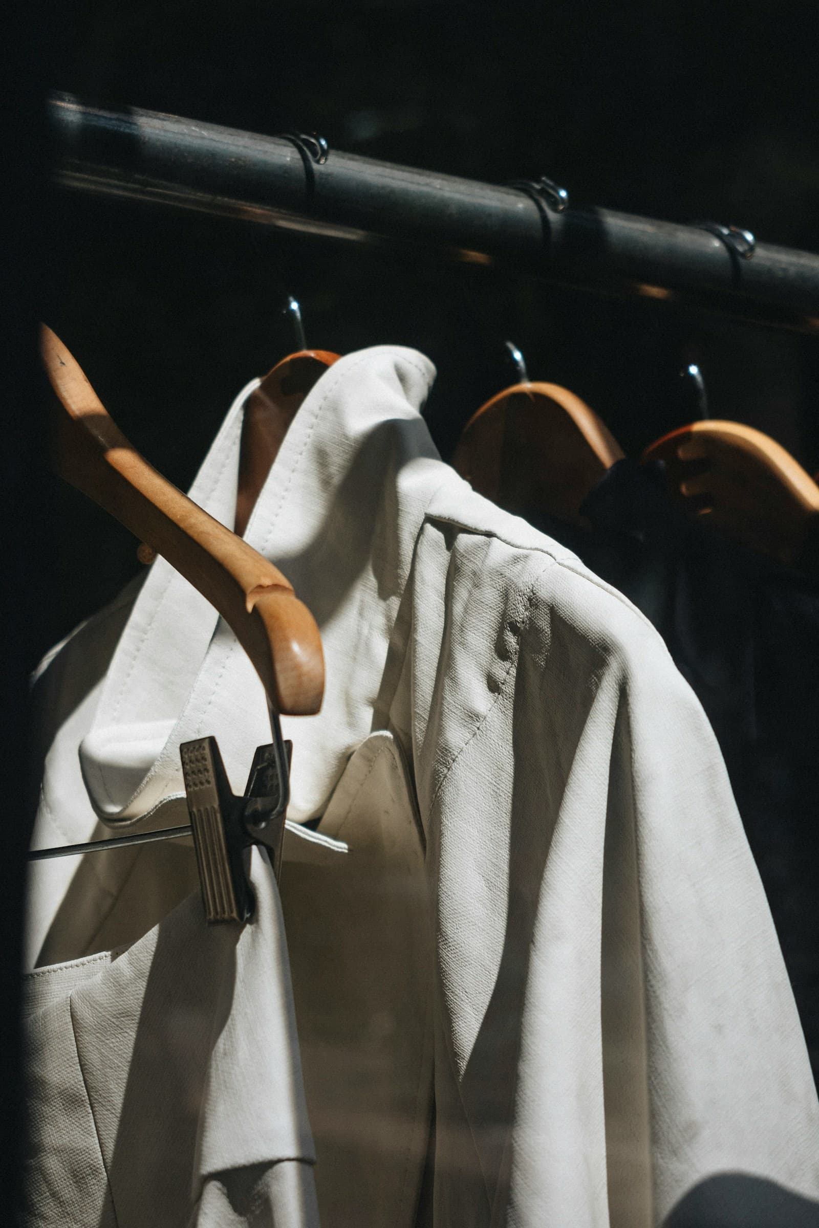 A light jacket hanging on a wooden hanger on a rail.