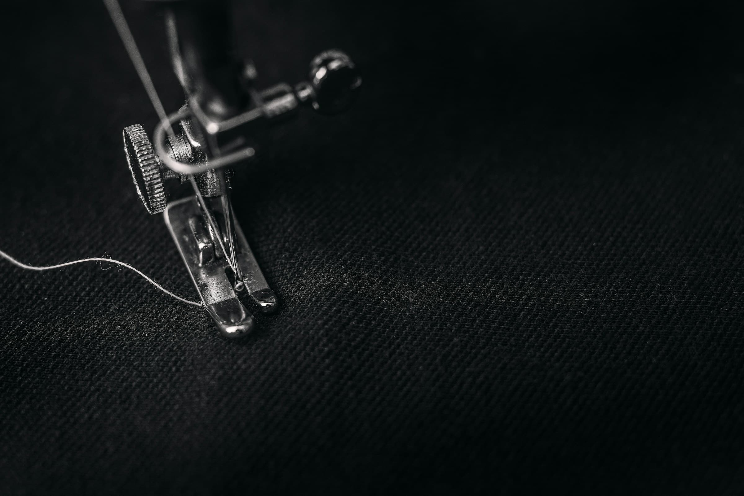 Macro: a sewing machine presser foot and a thread on dark fabric.